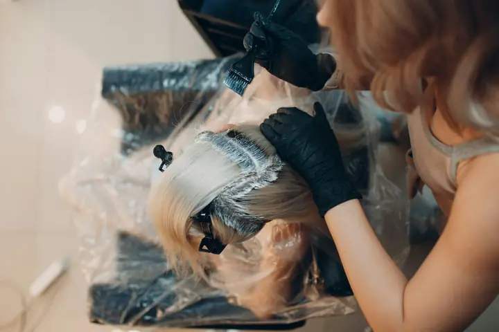 Mãos de luva preta aplicando descolorante com pincel.