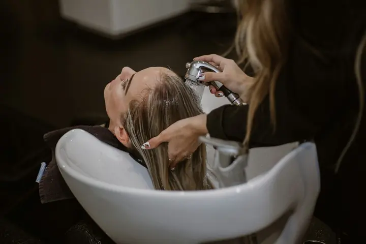 Cliente deitada no lavatório enquanto a cabeleireira lava o cabelo.