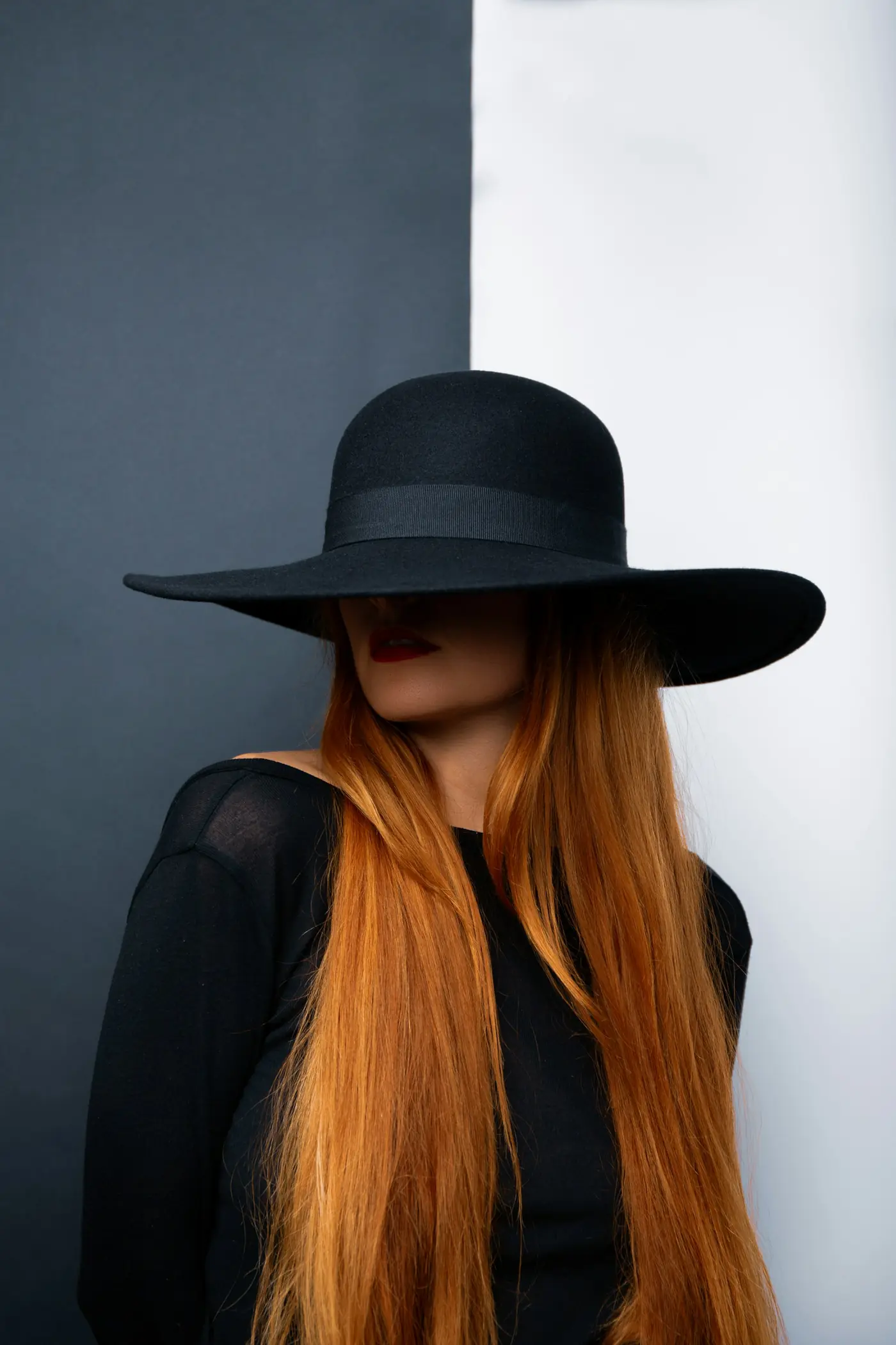 Mulher de chapéu preto com cabelo ruivo longo e liso até a cintura.