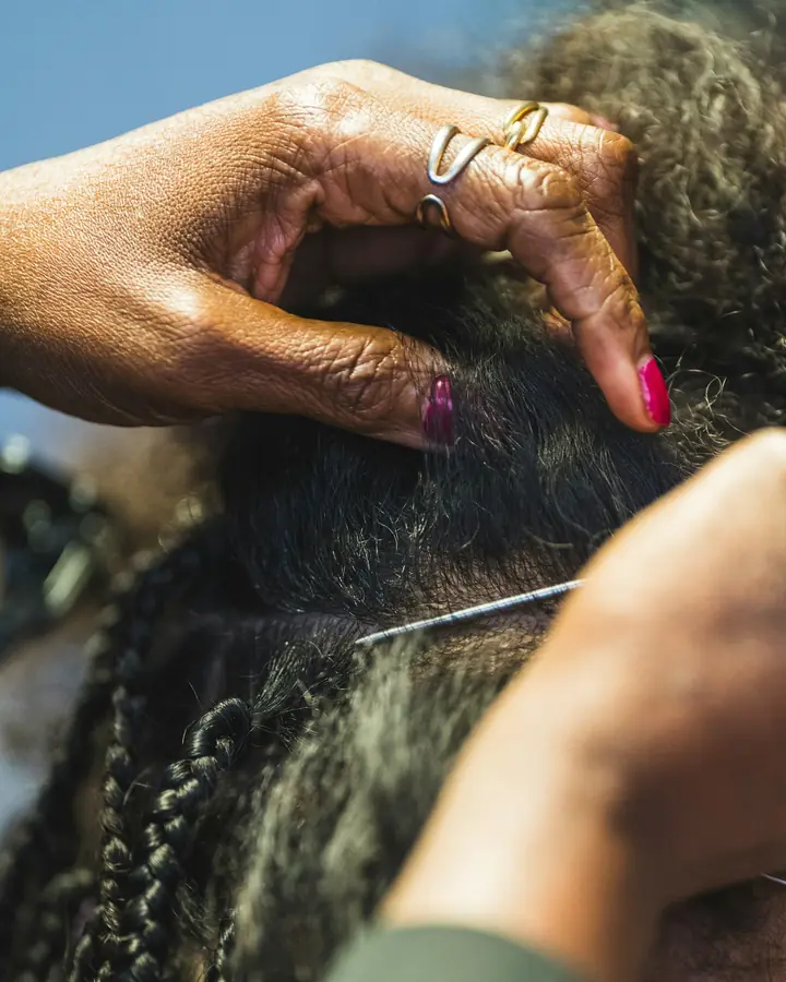 Mãos trançando cabelo crespo com uma agulha de crochê.